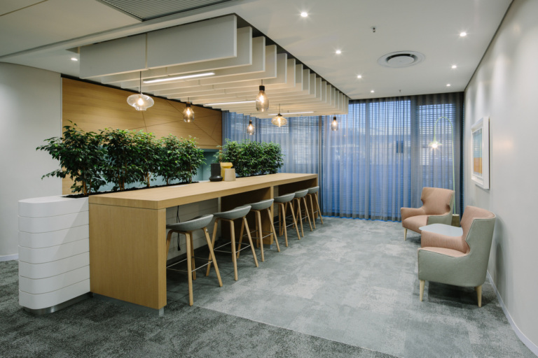 Elegant workplace lounge with timber counter, pendant lights, plants and soft seating by blue curtains