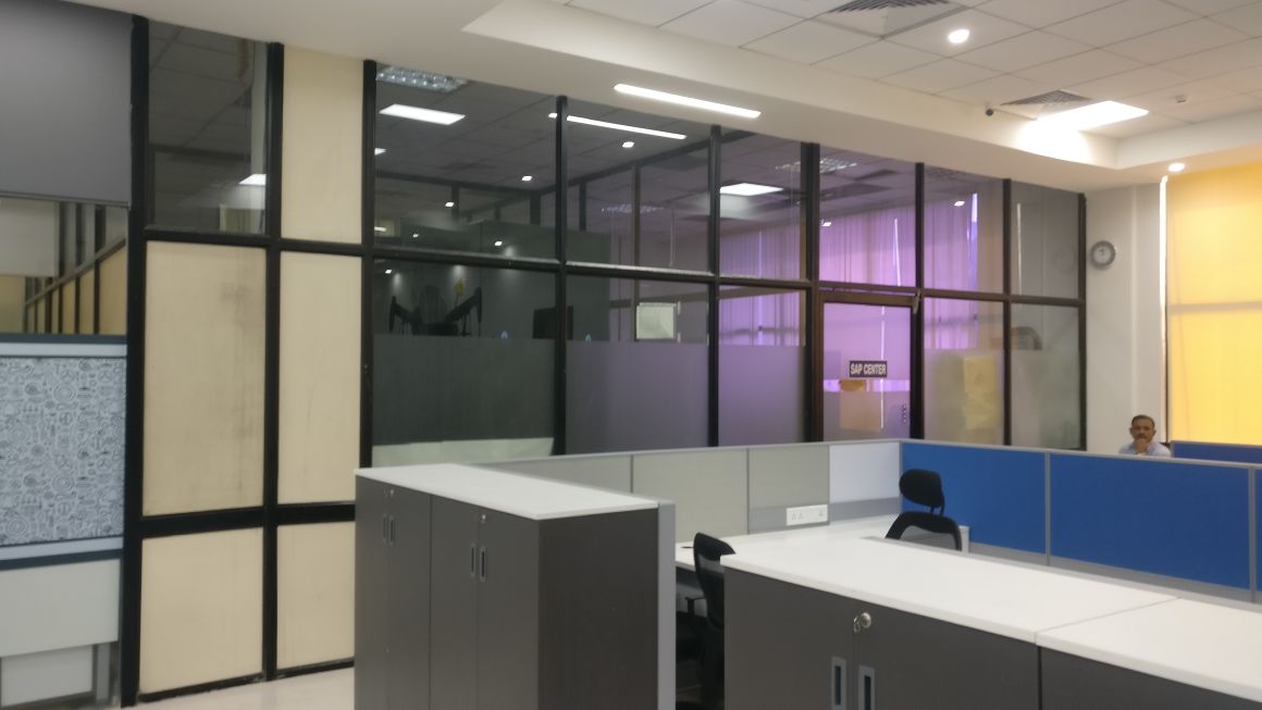 Minda Industries open-plan office with glass partition walls and purple-lit meeting pods beyond workstations