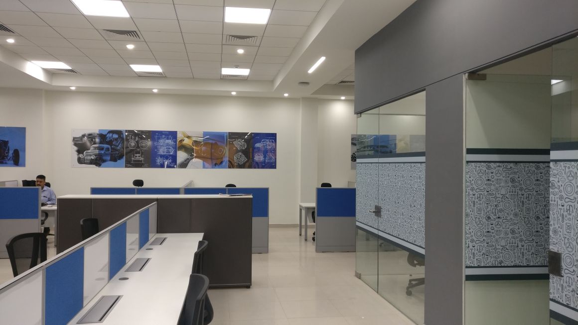 Minda Industries workspace with automotive blueprint wall art, blue workstations and graphic-printed glass partition