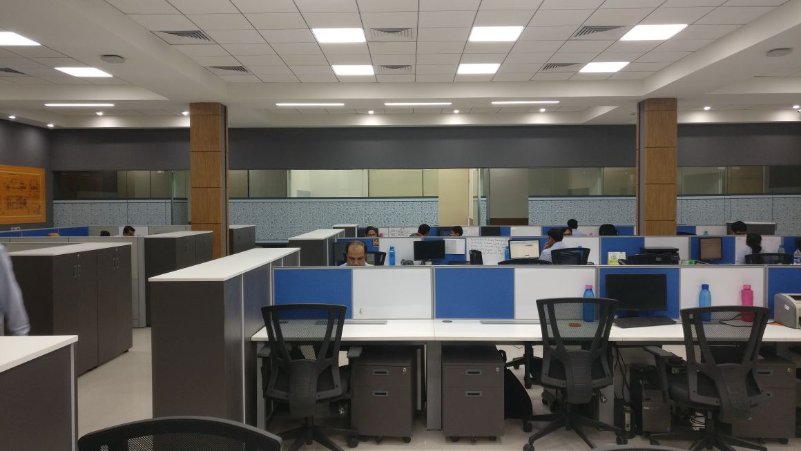 Large Minda office floor with blue-panel workstations, wooden columns and a mirrored ceiling band